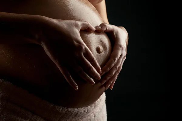 Les mains de la femme enceinte formant un cœur sur son ventre — Photo