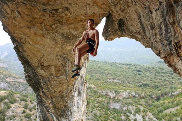 Scalatore di roccia appeso alla corda dopo aver raggiunto la cima del percorso, con pittoresche montagne sullo sfondo — Foto Stock