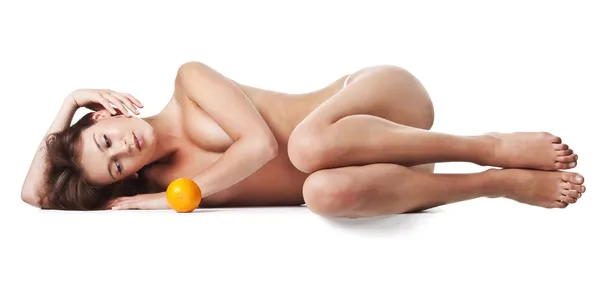 Mulher nua deitada de lado de pernas cruzadas com uma fruta laranja — Fotografia de Stock