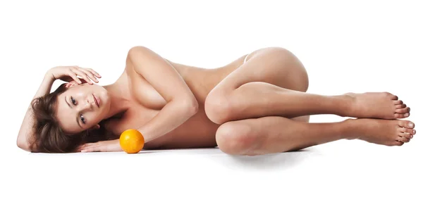 Donna nuda sdraiata sul fianco a gambe incrociate con un frutto arancione Immagini Stock Royalty Free