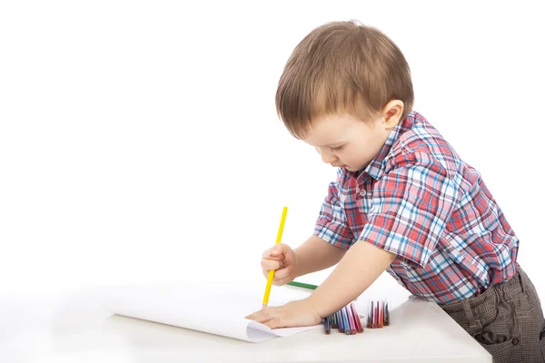 Un petit garçon à la table dessine avec des crayons de couleur Images De Stock Libres De Droits