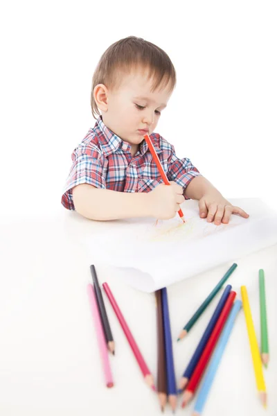Un petit garçon à la table dessine avec des crayons de couleur Photo De Stock