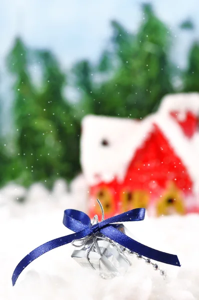Geschenk liegt im Schnee vor der Kulisse eines schneebedeckten Hauses — Stockfoto