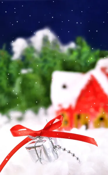 Подарок, лежащий в снегу на фоне заснеженного дома — стоковое фото