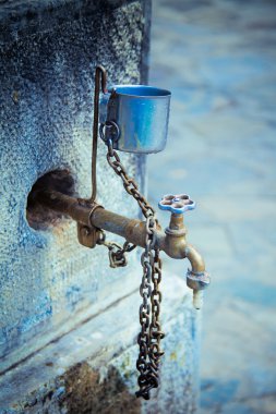 Vertical view of a old water tap with a metal cup. clipart