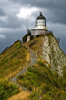 Nugget Point Light House and dark clouds in the sky clipart