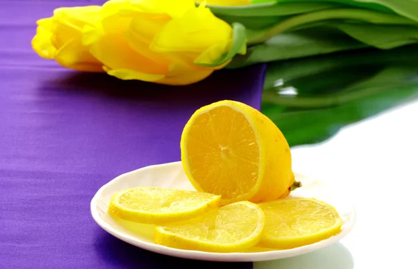 stock image Lemon on the white plate and some tulips on the table