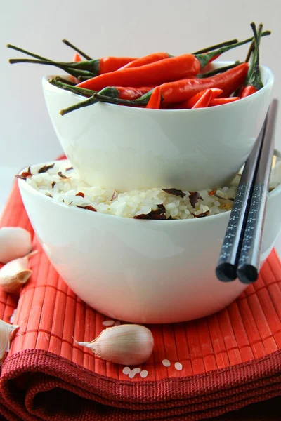 Bowls of uncooked rice and chili peppers — Stock Photo, Image
