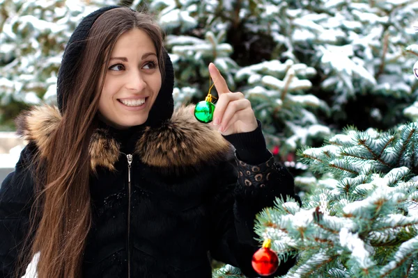 Pretty woman is standing beside a fir tree, smiles happy and holds a glass — Stock Photo, Image