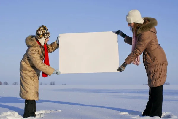 Girls holding white poster at winter snowy field — Stock Photo, Image