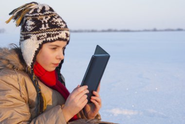 Teen girl reading e-book outdoors at winter time clipart