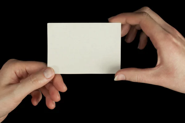 Mãos segurando um cartão branco isolado no fundo preto — Fotografia de Stock