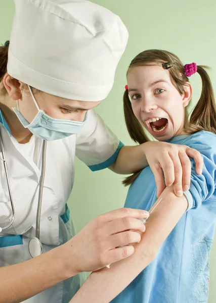 Lady doctor making an injection to scared teen girl Stock Picture