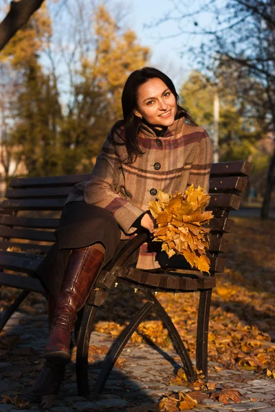 Mooie jonge vrouw op een bankje in de herfst — Stockfoto