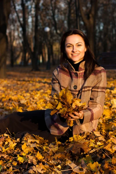 Hermosa joven sentada en hojas de otoño — Foto de Stock