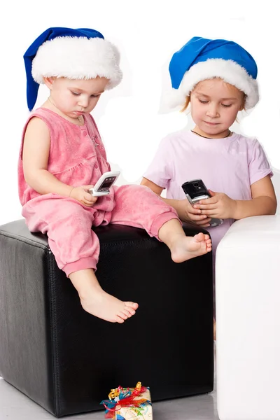 Duas crianças nos chapéus do Pai Natal enviando mensagens de saudação nos celulares — Fotografia de Stock