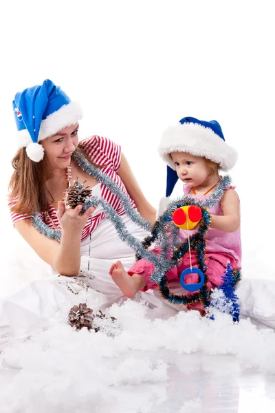 母亲和女儿在圣诞老人的帽子坐在人造雪 — 图库照片