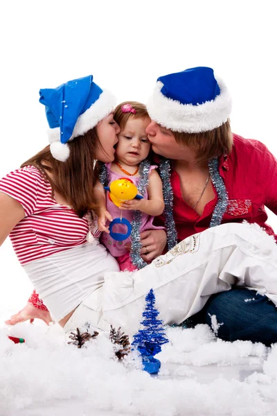 Parents in Santa's hat kissing their child in artificial snow — Stock Photo, Image