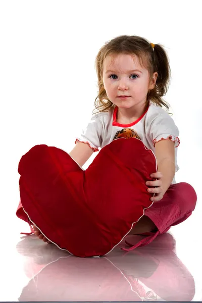 Vacker flicka sitter med hjärtat formade röd kudde — Stockfoto