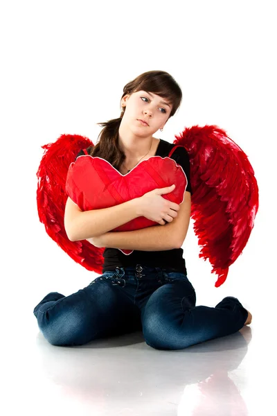 美丽的姑娘坐在一起的心状红色枕头中红色的天使翅膀上白色隔离 — 图库照片