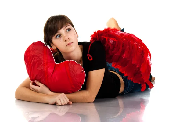 Vacker flicka liggande med hjärtat formade röd kudde i röda änglavingar — Stockfoto