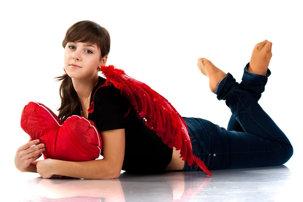 Vacker flicka liggande med hjärtat formade röd kudde i röda änglavingar — Stockfoto