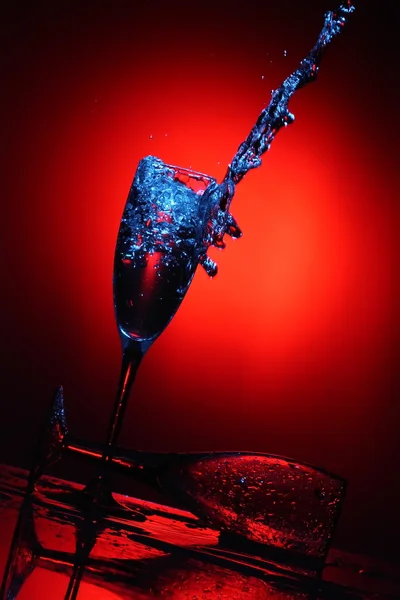 stock image Splashing water from the cup on a red background