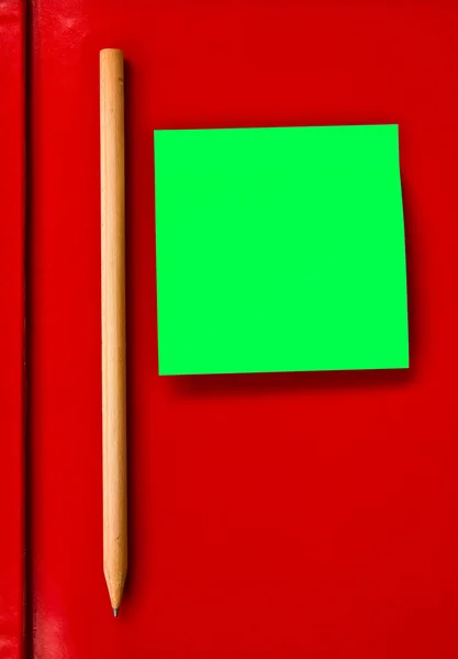Green note and pencil on red notebook — Stock Photo, Image