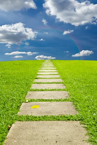 Lopen steen op gras naar hemel en regenboog — Stockfoto