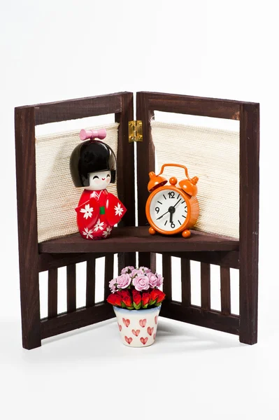 Japanische Puppe und orangefarbene Uhr auf Blumenständer — Stockfoto