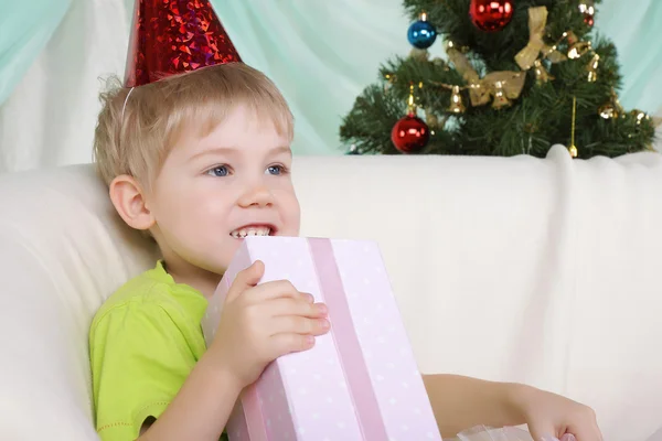 Маленький мальчик рядом с рождественской елкой сидит с подарком — стоковое фото