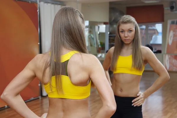 Девушка смотрит в зеркало спортзал в помещении — стоковое фото
