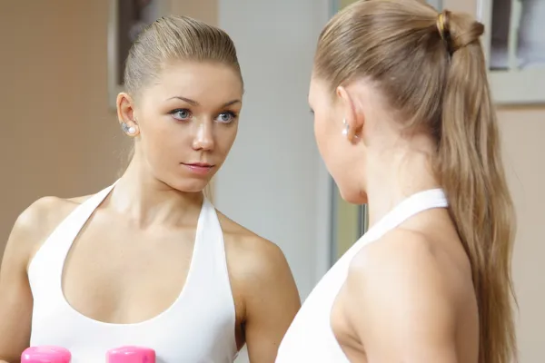 Hermosa chica rubia mirando en espejo gimnasio de fitness — Foto de Stock