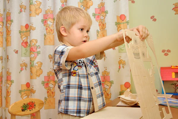 The little boy collects a wooden model sailboat — Stock Photo, Image