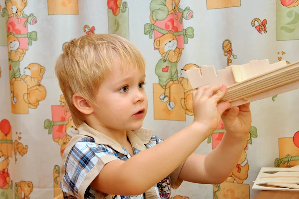 The little boy collects model wooden sailboat — Stock Photo, Image