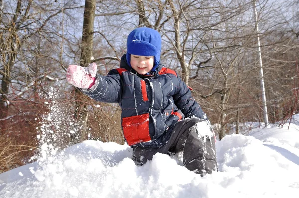 A little boy on a big snowdrift in winter snow throws. — Stock Photo, Image
