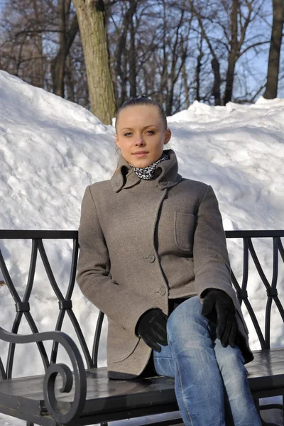 Uma linda garota está sentada em um banco de parque. Dia de sol — Fotografia de Stock