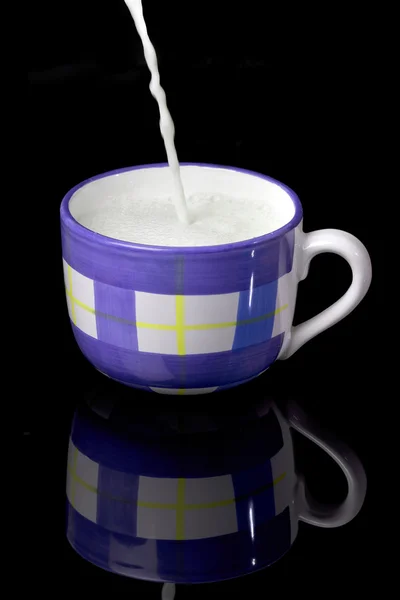 Latte fresco con schiuma che viene versata sulla tazza blu e bianca — Foto Stock