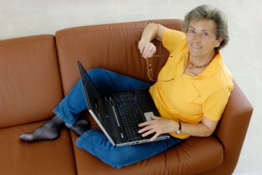 Senior woman with laptop on a couch clipart