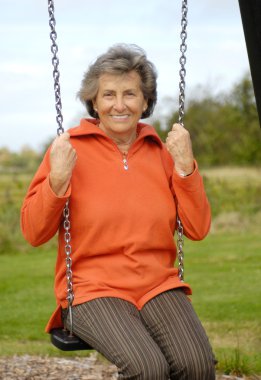 Senior woman on a playground swing clipart