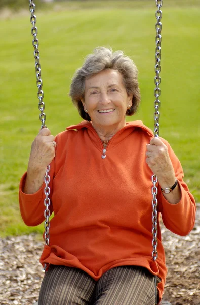 Starszy kobieta na plac zabaw huśtawka — Zdjęcie stockowe