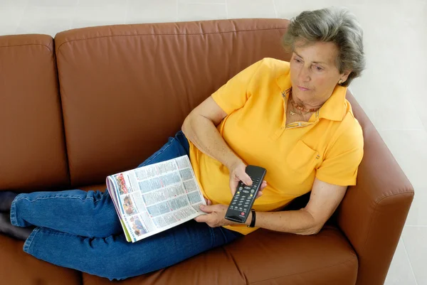 Ανώτερος γυναίκα με tv-απομακρυσμένου ελέγχου σε έναν καναπέ — Φωτογραφία Αρχείου