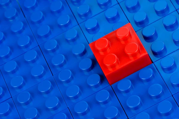 Red building block in a field of blue one — Stock Photo, Image