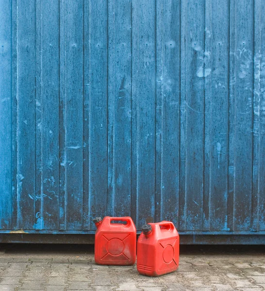 Iki kırmızı benzin kutu mavi konteyner duvarın önünde — Stok fotoğraf