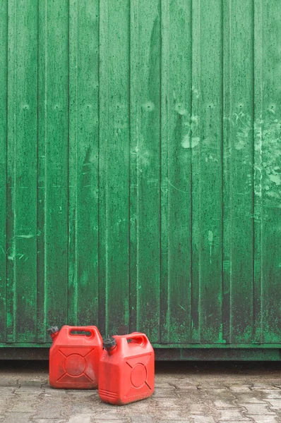 Dos latas de gasolina roja frente a una pared de contenedores verdes — Foto de Stock