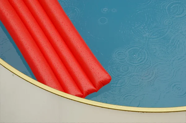Red airbed in a swimming pool in the rain — Stock Photo, Image