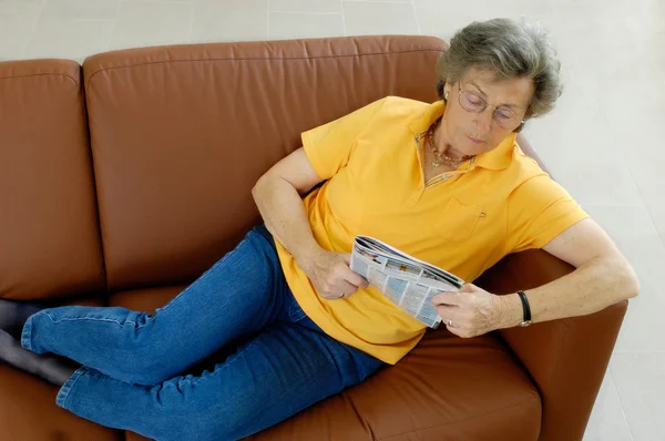 stock image Senior woman with tv-magazine on a couch