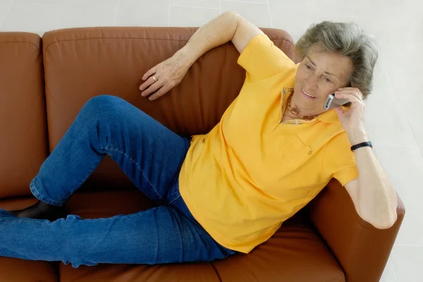 Ανώτερος γυναίκα με το κινητό τηλέφωνό σας σε έναν καναπέ — Φωτογραφία Αρχείου