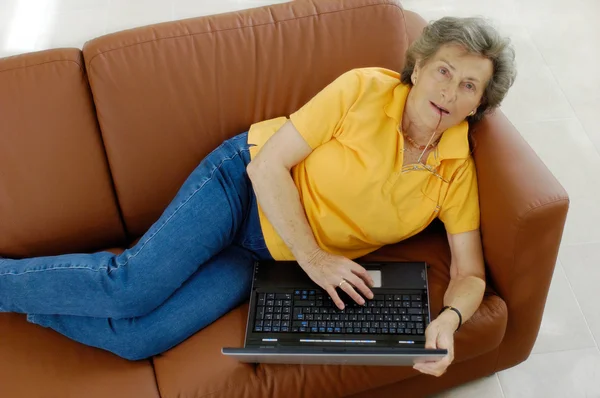 Ανώτερος γυναίκα με φορητό υπολογιστή σε έναν καναπέ — Φωτογραφία Αρχείου