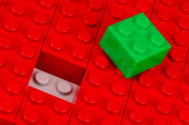 Green building block in a field of red ones clipart